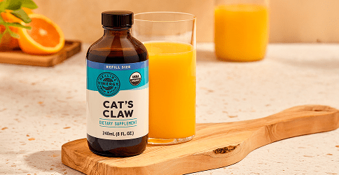 Cat's Claw supplement bottle with a glass of orange juice on a wooden board.